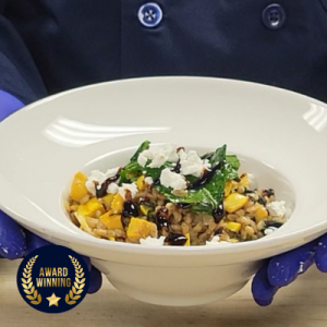 Delicata Farrotto with Balsamic Gastrique & Goat Cheese in a white bowl held by chef