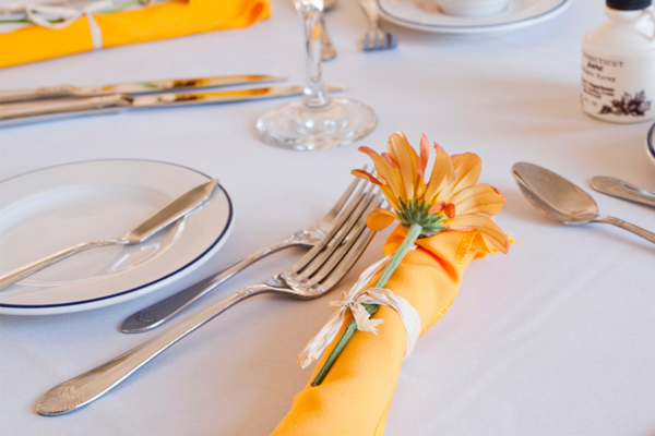table with a white table cloth, formal place setting, yellow napkin and flower