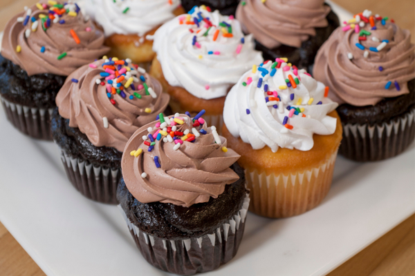 plate of yellow and chocolate cupcakes with white frosting and sprinkles