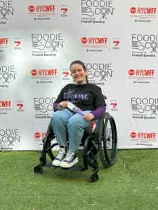 Photo of Gabby DiSalvo in her wheelchair in front of a step and repeat backdrop