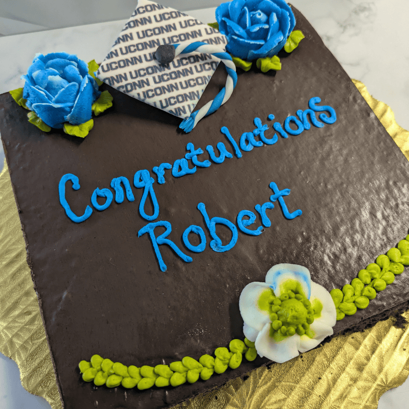 Chocolate mousse cake that says Congratulations Robert and is decorated with flowers and a UConn-branded mortar board and tassel