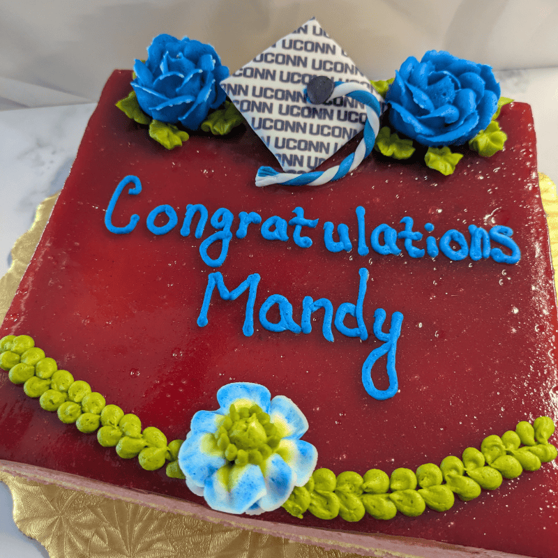 Raspberry mousse cake that says Congratulations Mandy and is decorated with flowers and a UConn-branded mortar board and tassel