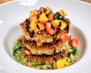stack of panko breaded eggplant discs layered with bruschetta surrounded by a base of beans and pesto in a white bowl