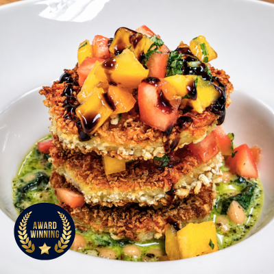 stack of panko breaded eggplant discs layered with bruschetta surrounded by a base of beans and pesto in a white bowl